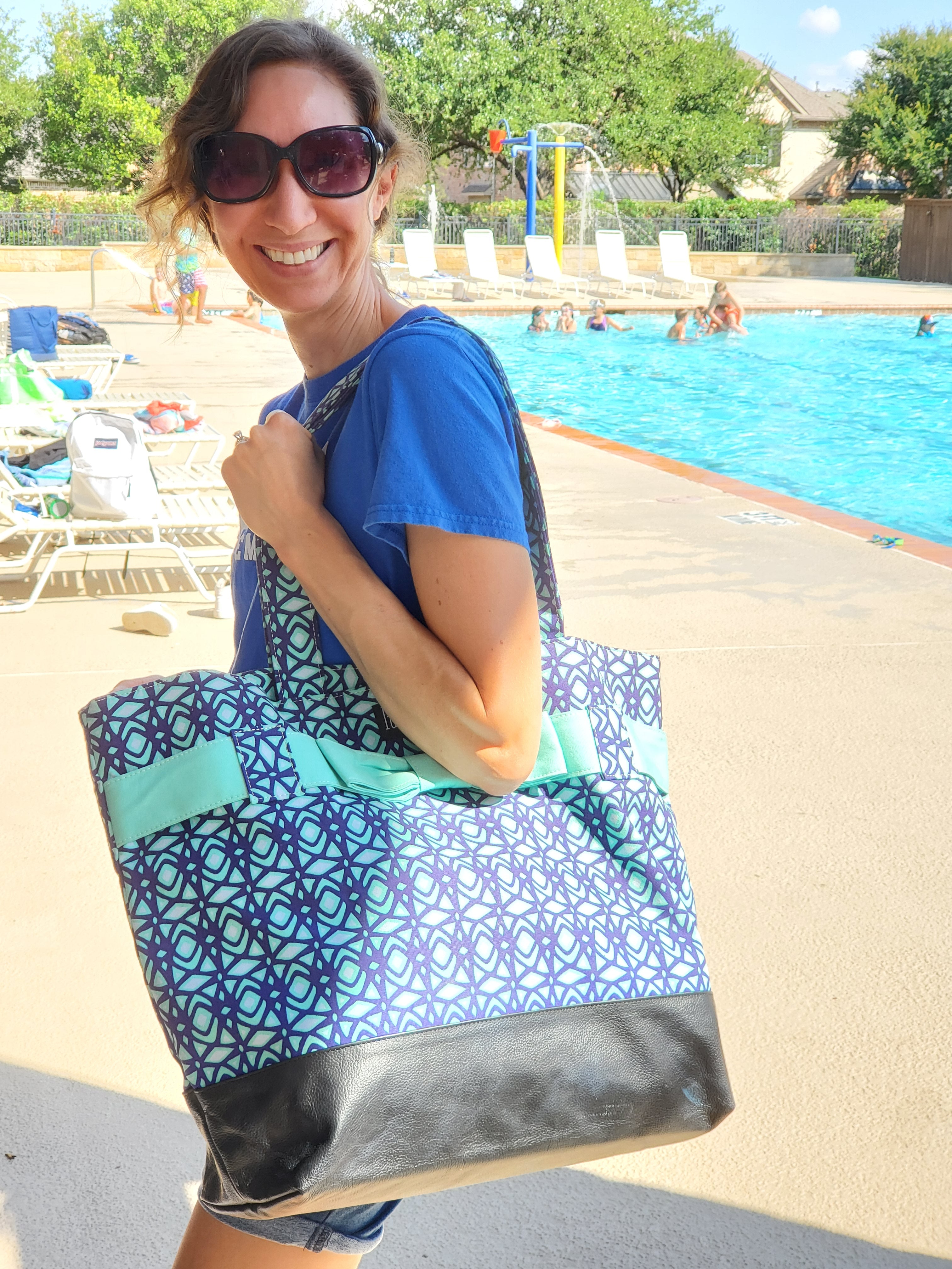Woman holding large blue beach tote by the pool.