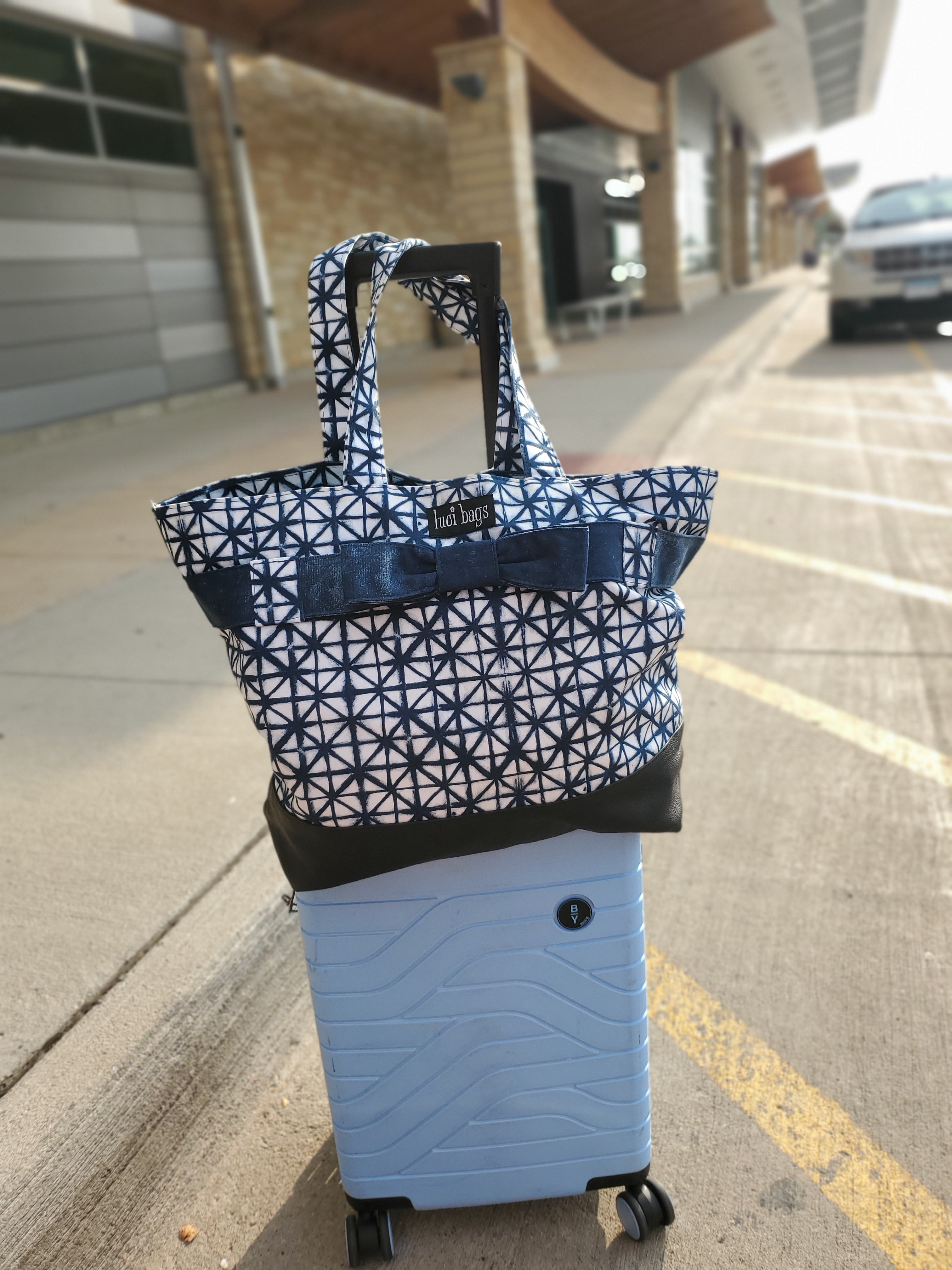 Large blue and white shibori tote sitting on top of suitcase at the airport.