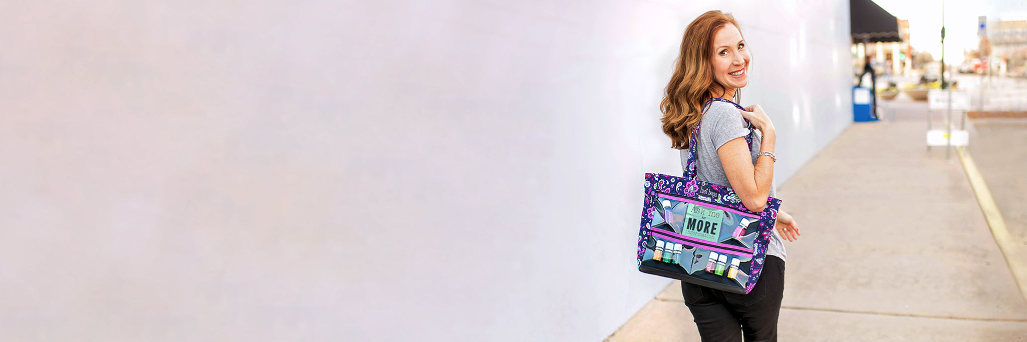 Woman walking down street with purple paisley display tote featuring essential oils.