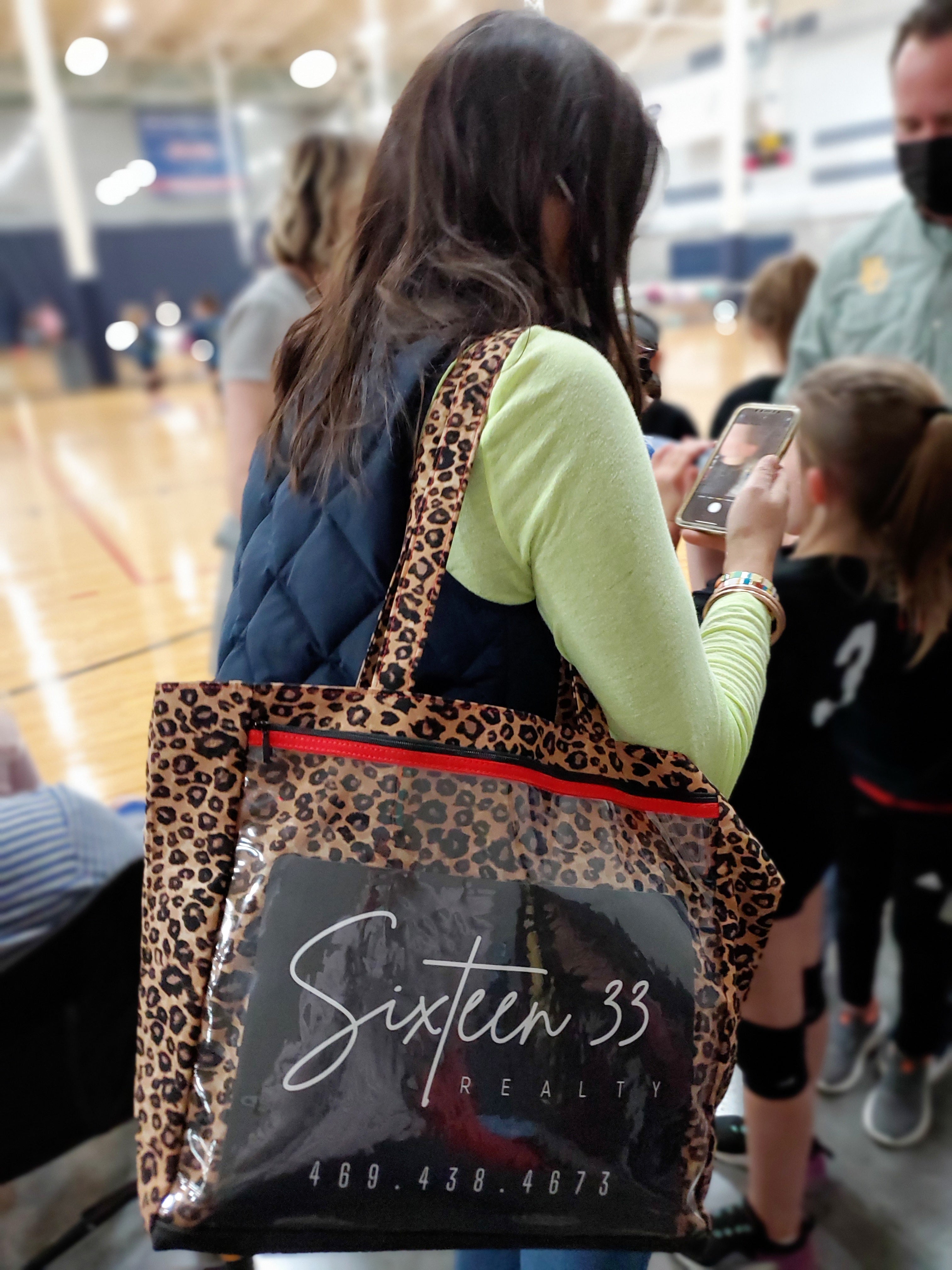 Woman on phone at a sporting event holding a leopard tote marketing her reality business.